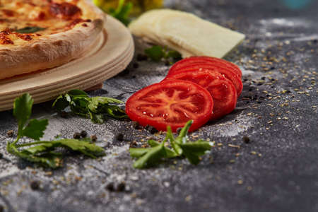 Whole and cutted tomato in ingredients of pizza on italian black paper tableの写真素材