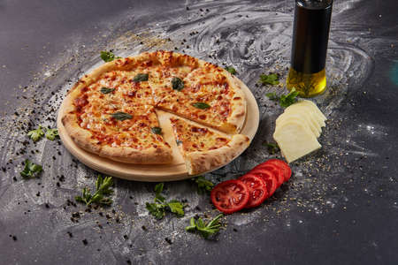 whole italian pizza on wood table with ingredients in black tableの写真素材