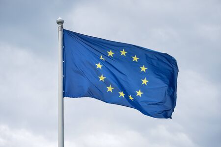 The flag of the European Union fluttering on wind against the background of gray clouds.の写真素材