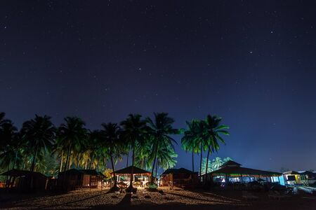 Coastal cafes, restaurants and beach lodges, in night illumination under the star sky, between the palms.の写真素材
