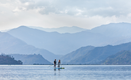 Standing paddleboarding (SUP-surfing) on ??the lake Pheva, in the Himalayas, against the background of the mountains thawing in a haze. March 3, 2017. Nepal. Pokhara.のeditorial素材