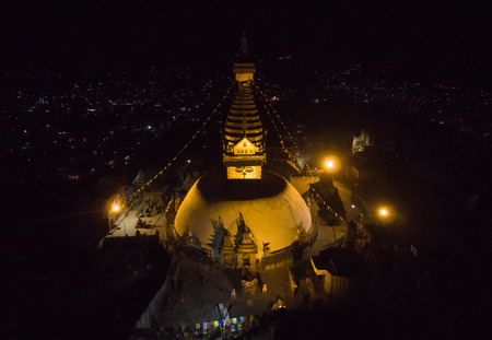 The top view of the sacred of the ancient stupa of Svayambhu shining gold in the night-time lighting of the searchlights over Kathmandu Valley.の写真素材