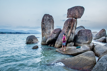 The man of the European appearance, fishes on a rod, standing on a big boulders in one of Agonda beach bays, the State of GOA, India, on February 24, 2014のeditorial素材