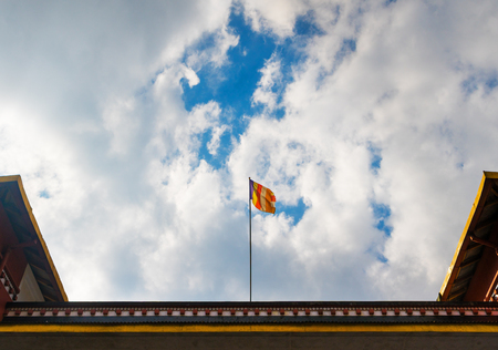Official flag of the Buddhism on a roof of the Buddhist temple against the background of the solar sky with cloudsの写真素材