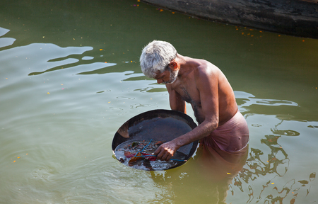 The elderly man with the gray-haired head looks for the useful or valuable things which are thrown out at cremation in coastal silt of Ganges. India, Varanasi, on February 6, 2014のeditorial素材