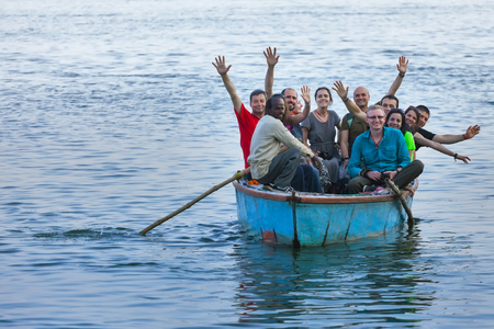 The company of young Europeans rides the old boat down the river Ganges and friendly waves a hand. India, Varanasi, on February 6, 2014のeditorial素材