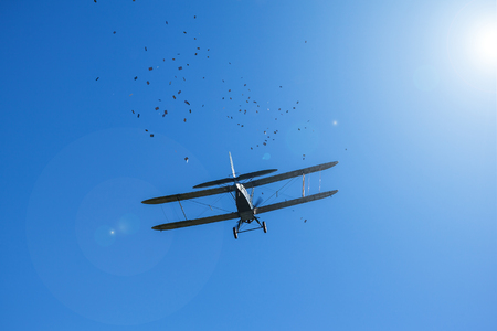 Flight old aeroplane-biplane and from him flies scatter handbills on the background of the blue sky in beams and reflections of spot of light from the sun.のeditorial素材