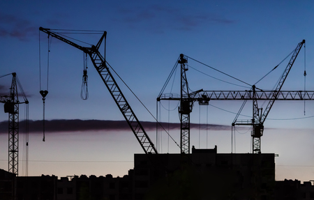 Silhouettes of construction cranes of different types and part of the building site against the background of the twilight sky after a dusk.の写真素材