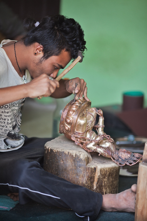 The master in creation of traditional Buddhist bronze statues at work. There is a stamping of decorative elements of Tara. Nepal, Kathmandu, on March 7, 2017.のeditorial素材