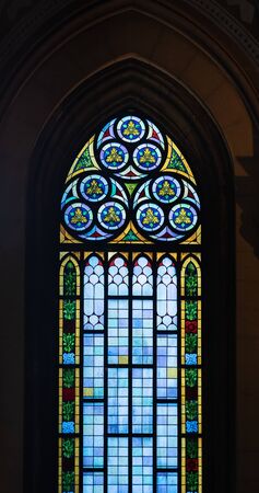 A high stained glass window with colored accents in an old Catholic church.