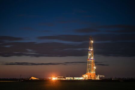 The derrick used for investigations of the gas field in beams of searchlights against the background of the cloudly evening dark sky.の写真素材