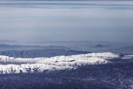 An aerial view of the mountain ranges covered with snow, gorges and valleys of part of the Iranian Highlands, gradually dissolving in the haze and merging with the horizon.の写真素材
