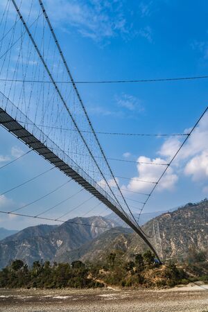 A big suspension pedestrian bridge crossing a rough mountain river in the Himalayas. View from underbridge.の写真素材