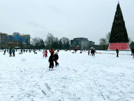 Adults and children skate on ice around a Christmas treeの写真素材