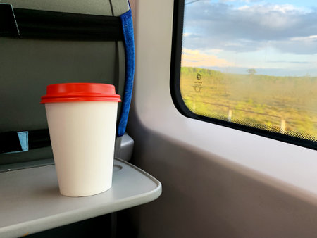 Disposable Glass in the Train near the window. Cardboard white Cup with a hot drink on the table....