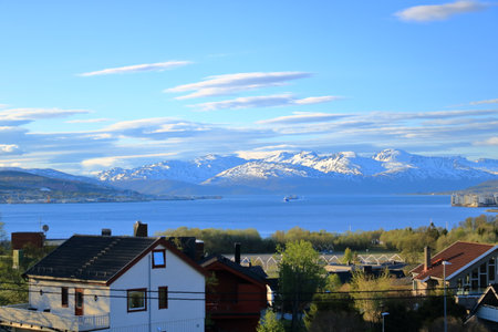 May 28 2022 - Tromso in Norway: Ships approach the port, Snowy mountains in the backgroundのeditorial素材
