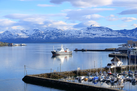 May 28 2022 - Tromso in Norway: Ships approach the port, Snowy mountains in the backgroundのeditorial素材