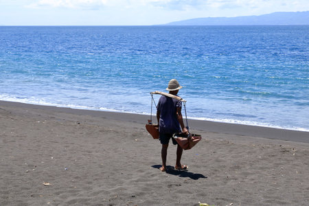 Kusamba, Bali in Indonesia - February 08 2024: Farmer collecting water in the sea, to salt field for...