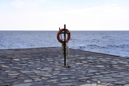 an Orange lifebuoy hanging on a pole in a volcanic landscape, Muelle de Orchilla, El Hierro, Canary islands, Spainの写真素材