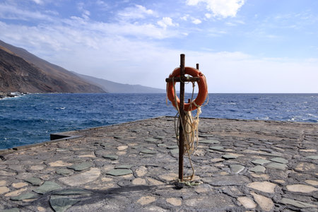 an Orange lifebuoy hanging on a pole in a volcanic landscape, Muelle de Orchilla, El Hierro, Canary islands, Spainの写真素材