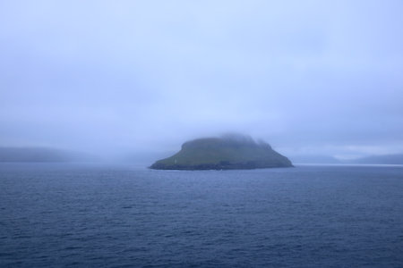 dramatic island emerges from the tranquil waters of the Faroe Islands, shrouded in a thick layer of fogの写真素材