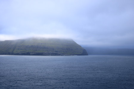 dramatic island emerges from the tranquil waters of the Faroe Islands, shrouded in a thick layer of fogの写真素材