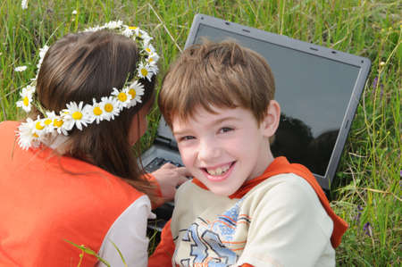 a pigeon pair lie on a green grass among the field colors and look in the screen of notebookの写真素材