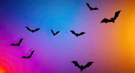 Halloween background with flying bats silhouettes over colorful sunset sky.