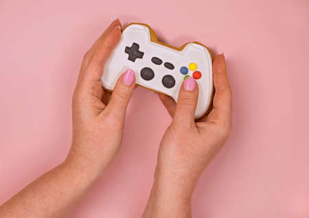 female hands hold a gingerbread in the form of a game console on a pink backgroundの写真素材