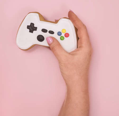 female hand holds gingerbread shaped game console on pink backgroundの写真素材