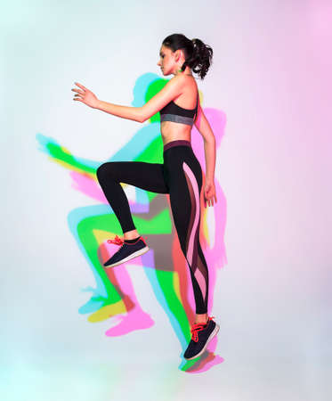 attractive woman doing stretching exercise or yoga moves with glitch duotone effect. Young sporty model at studio and double colourful shadowsの写真素材