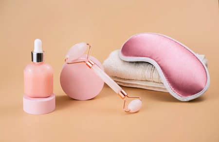 gentle background for cosmetics product presentation with rose quartz massage roller, sleeping mask and  bottle of cosmetic oil or serum. evening routine before bedtime, beauty treatments to keep skin freshの写真素材