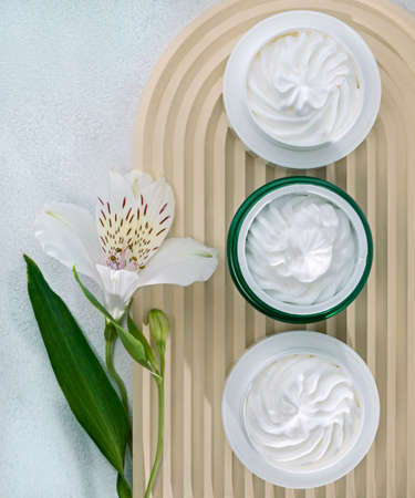 open cosmetic jars with nourishing or moisturizing cream on a corrugated beige background and alstroemeria flowerの写真素材