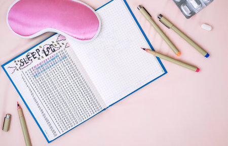 Sleeping mask, alarm clock and sleep tracker journal on pink pastel background. How to Use a Sleeping Log to Diagnose Insomniaの写真素材