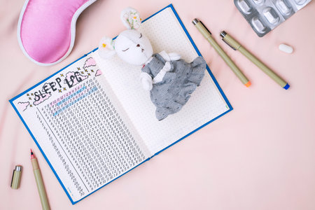 Sleeping mask, alarm clock and sleep tracker journal on pink pastel background. How to Use a Sleeping Log to Diagnose Insomniaの写真素材