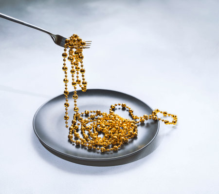 a fork with a string of decorative beads in a dark plate on a light table. Creative concept, consumerismの写真素材