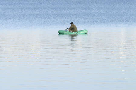 Fisherman within green rubber boat in a lake