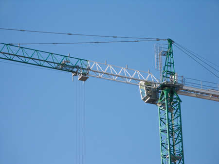 Green and white construction hoisting crane over clear blue skyのeditorial素材
