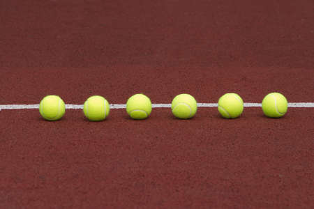 Six yellow tennis balls in-line on court with synthetic surfaceの写真素材