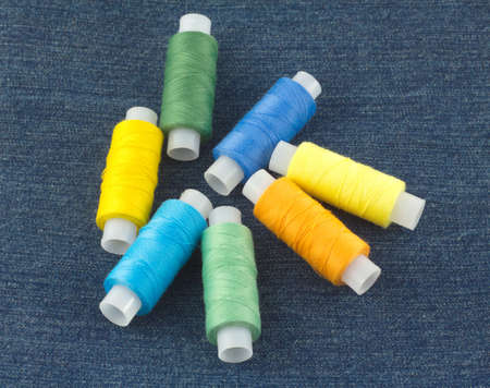 Spools with color threads on blue jeans fabric close up