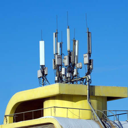 Many electronics aerials on yellow building top over blue cloudless skyの写真素材