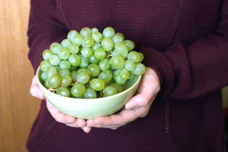 Female hands hold green  bowl with appetizing grape closeupの写真素材
