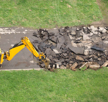 Heavy road construction machine breaks up old asphalt with hammerの写真素材