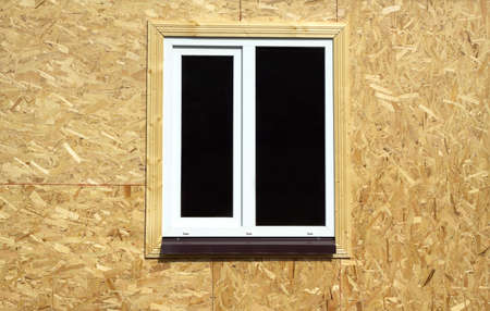 Wall from wooden panels made of pressed sandy brown wood shavings with white plastic window in a new house closeupの写真素材