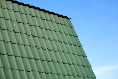 Part of new country house roof from green metal tile against blue cloudless skyの写真素材
