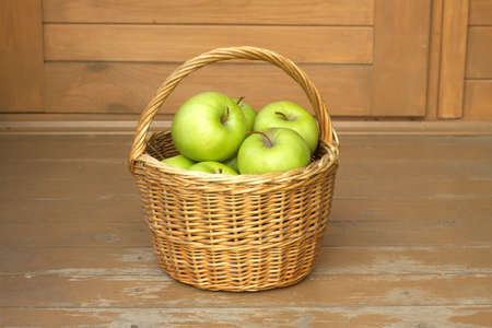 Still life with green apples in brown wicker basket on timber background closeup. Horizontal viewの写真素材
