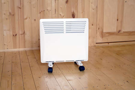 White electric convector heater with horizontal louvers in wooden house roomの写真素材