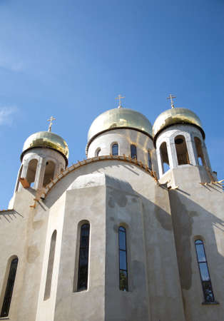 Construction of a new temple with gold domes against blue sky with light white clouds. Vertical...