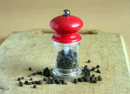 Still life with black peppercorn and manual mill with red cap, standing on wooden kitchen board. Photo closeupの写真素材