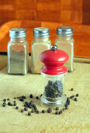 Still life with black peppercorn, hand mills with red cap and three glass spice jars on kitchen table. Photo closeupの写真素材